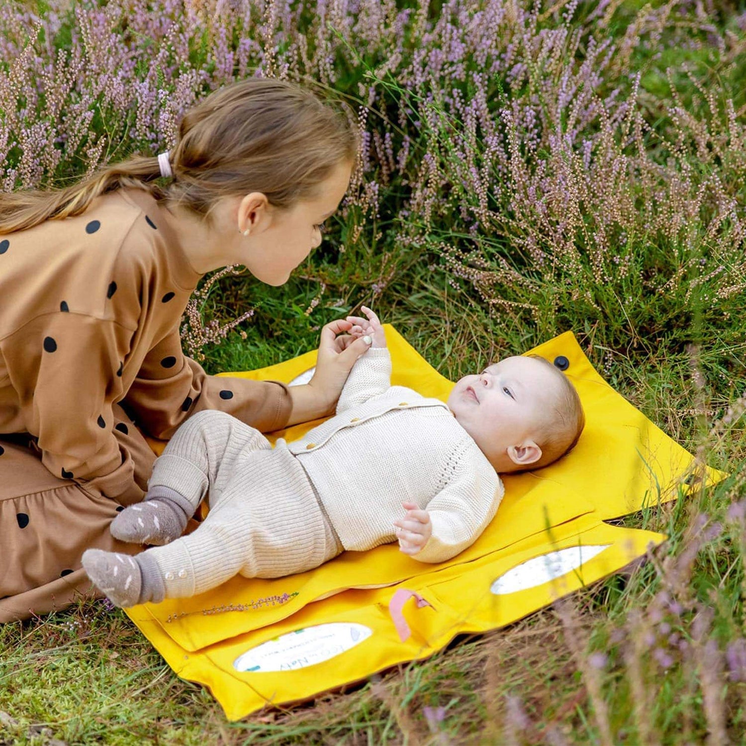 Ein Baby liegt auf der ausgefalteten Wickeltasche von Villawind auf einer Wiese