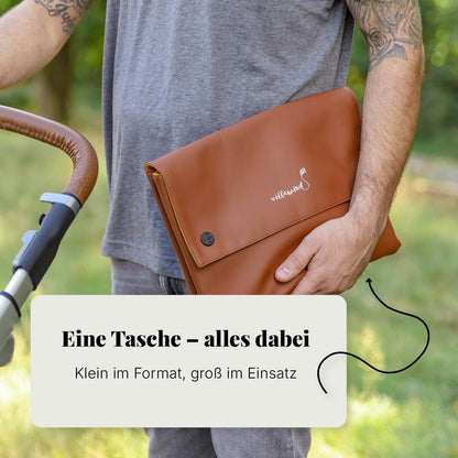 Vater trägt kompakte Villawind Wickeltasche unter dem Arm neben Kinderwagen